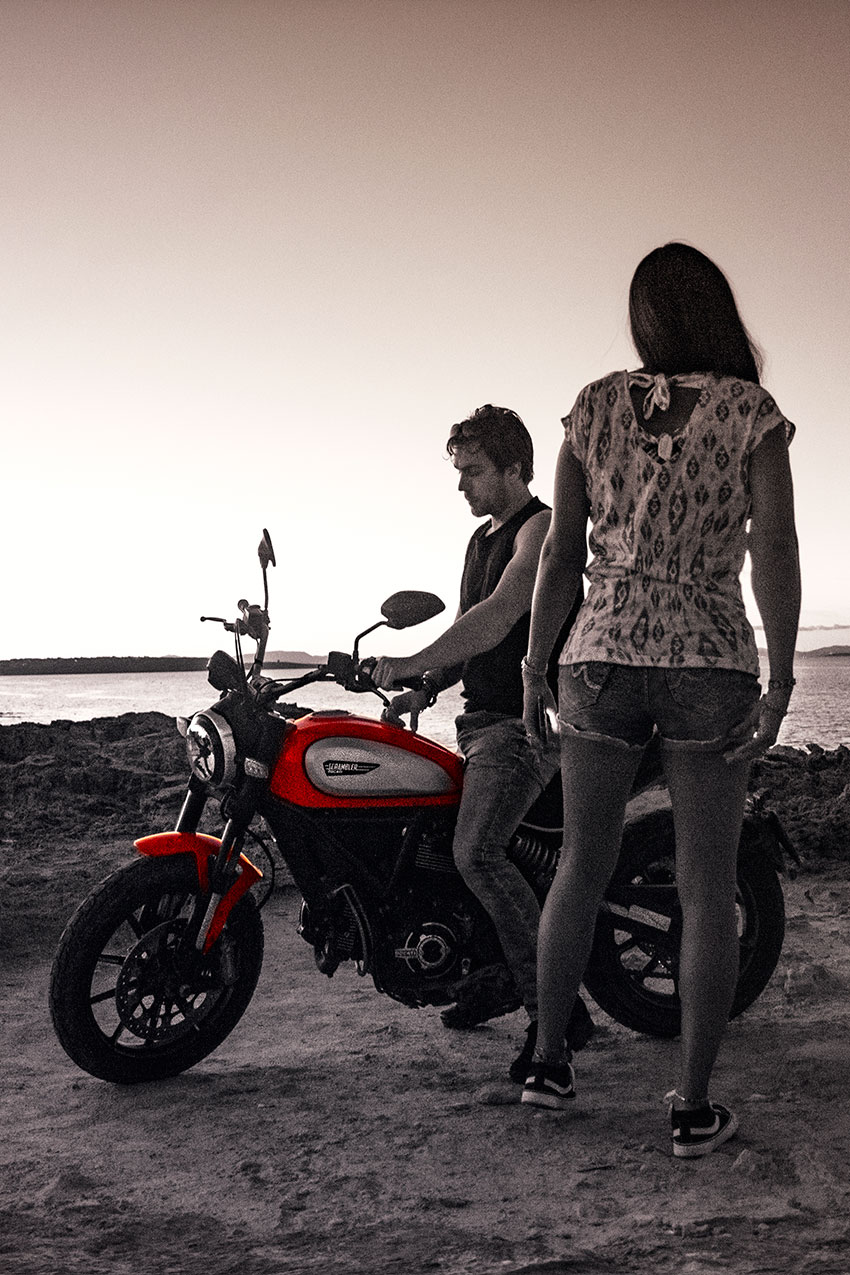 Black and white photography of a couple riding a motorcycle at Es Calo beach, Formentera, Spain, (Nos Dren).