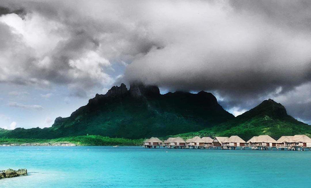 French Polynesia, Bora Bora island, mount Otemanu under clouds with high constrat, behind the blue lagoon and the stilt houses. (Nos Dren)
