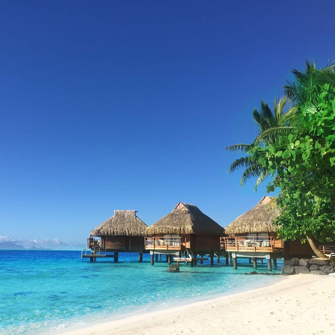 French Polynesian island Tikehau with paradise beach of white sand, palm trees, crystal blue water and stilt houses. (Nos Dren)